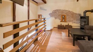 A cozy living room with a stone wall, wooden beams, a fireplace, and a TV mounted on the wall. - Apartment Near the Forest in Meisburg (Meisburg)