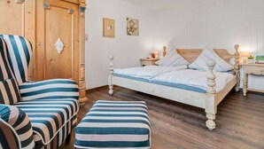 A bedroom with a wooden bed, a striped armchair, and a matching ottoman. - Apartment Near the Forest in Meisburg (Meisburg)