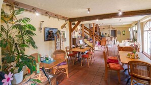 A cozy, rustic dining area with wooden furniture, potted plants, and a staircase leading to an upper level. - Apartment Near the Forest in Meisburg (Meisburg)
