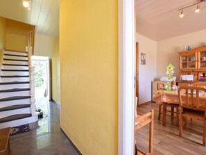 Una escala condueix a una habitació amb una paret groga, una taula de menjador de fusta i un armari amb portes de vidre.