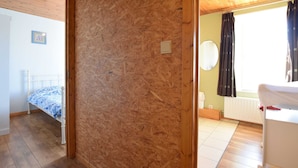 Ein Zimmer mit Holzboden, einem Bett mit gemustertem Überwurf, einer Holzwand und einem Fenster mit Vorhängen.