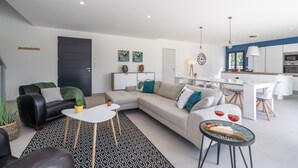 A modern living room with a sofa, coffee table, and dining area. - Holiday Home Beaufort With Private Pool (Beaufort)