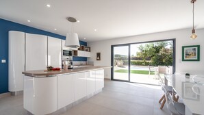 A modern kitchen with a central island, built-in appliances, and a dining area with a glass table. - Holiday Home Beaufort With Private Pool (Beaufort)