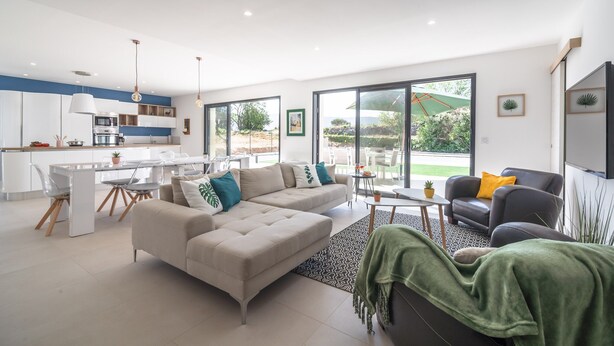A modern living room with a sofa, armchair, and coffee table, connected to a kitchen and dining area. - Holiday Home Beaufort With Private Pool (Beaufort)