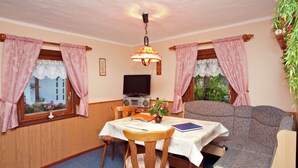 A cozy room with a dining table, chairs, a sofa, a television, and a ceiling light fixture. - Holiday Home in the Forest (Schmogrow)