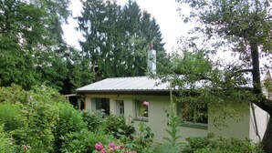 A small house with a green roof, surrounded by dense greenery and flowering plants. - Ferienhaus, Wernigerode (Wernigerode)