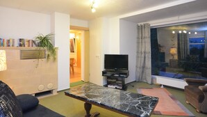 A living room with a flat-screen TV, a marble coffee table, a sofa, a bookshelf, and a large window with curtains. - Ferienhaus, Wernigerode (Wernigerode)