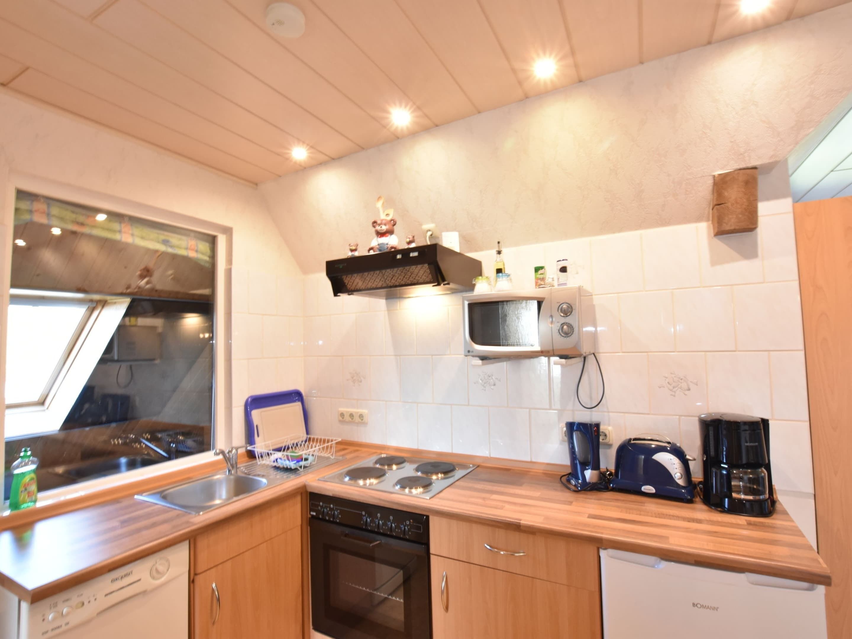 A compact kitchen with wooden cabinets, a built-in microwave, a coffee maker, and a dishwasher.