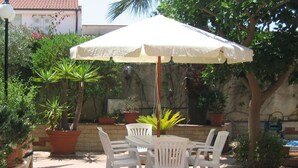 An outdoor patio with a white table and chairs under a large umbrella, surrounded by potted plants and a stone wall. - Simplistic Holiday Home in Sciacca near Horse Riding (Sciacca)