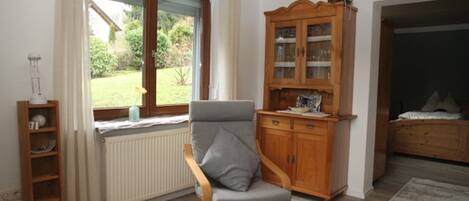 Une pièce comprenant une chaise en bois, un meuble avec des portes en verre, un radiateur et une fenêtre donnant sur un paysage verdoyant.