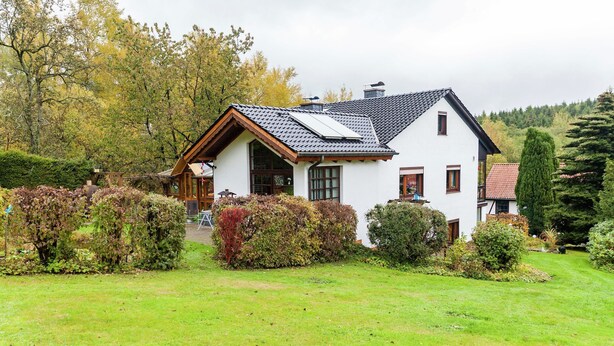 A white house with a sloped roof and a small porch, surrounded by a well-maintained garden and trees. - Amazing Apartment in Großalmerode near Cross Country Skiing (Grossalmerode)