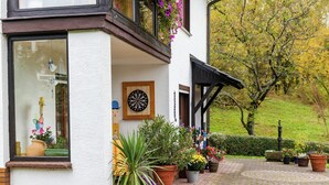 A building with a white exterior, a wooden door, and a window with a vase and flowers. There are potted plants in front of the building. - Amazing Apartment in Großalmerode near Cross Country Skiing (Grossalmerode)