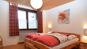 A wooden bed in a room with a radiator, a window with curtains, a wall-mounted light, and a painting. - Quiet Holiday Home With Terrace (Korbach)
