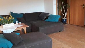 A living room with a dark grey sofa, teal cushions, a wooden coffee table with a flower arrangement, and a potted plant. - Quiet Holiday Home With Terrace (Korbach)