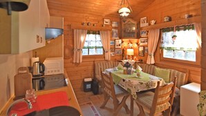A cozy cabin interior with wooden walls, a dining table set with chairs, a kitchen area with appliances, and a hanging light fixture. - Large Holiday Home in Battenhausen With Garden (Haina)