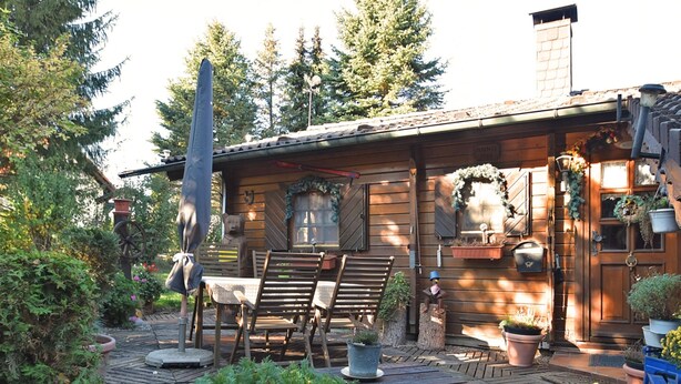 A rustic wooden cabin with a patio area featuring a wooden table and chairs, surrounded by potted plants and a large umbrella. - Large Holiday Home in Battenhausen With Garden (Haina)