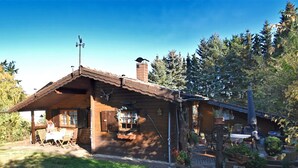 A rustic wooden cabin with a sloped roof, a porch with outdoor seating, and a chimney. - Large Holiday Home in Battenhausen With Garden (Haina)