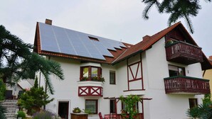 Una casa de dos pisos con techo inclinado, paneles solares y un balcón con barandilla de madera.