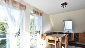 A dining area with a table and chairs, a kitchen with cabinets, and a window with curtains. - 4 Room Holiday Apartment with Garden near Lake (Lebrade)
