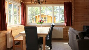 A wooden cabin interior with a dining table, chairs, a bench, a sofa, and a view of a wooden house outside. - Ferienhaus, Wissinghausen (Medebach)