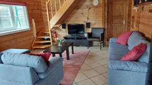 A cozy living room with a wooden staircase, a flat-screen TV, a coffee table, and two grey sofas with red cushions. - Ferienhaus, Wissinghausen (Medebach)