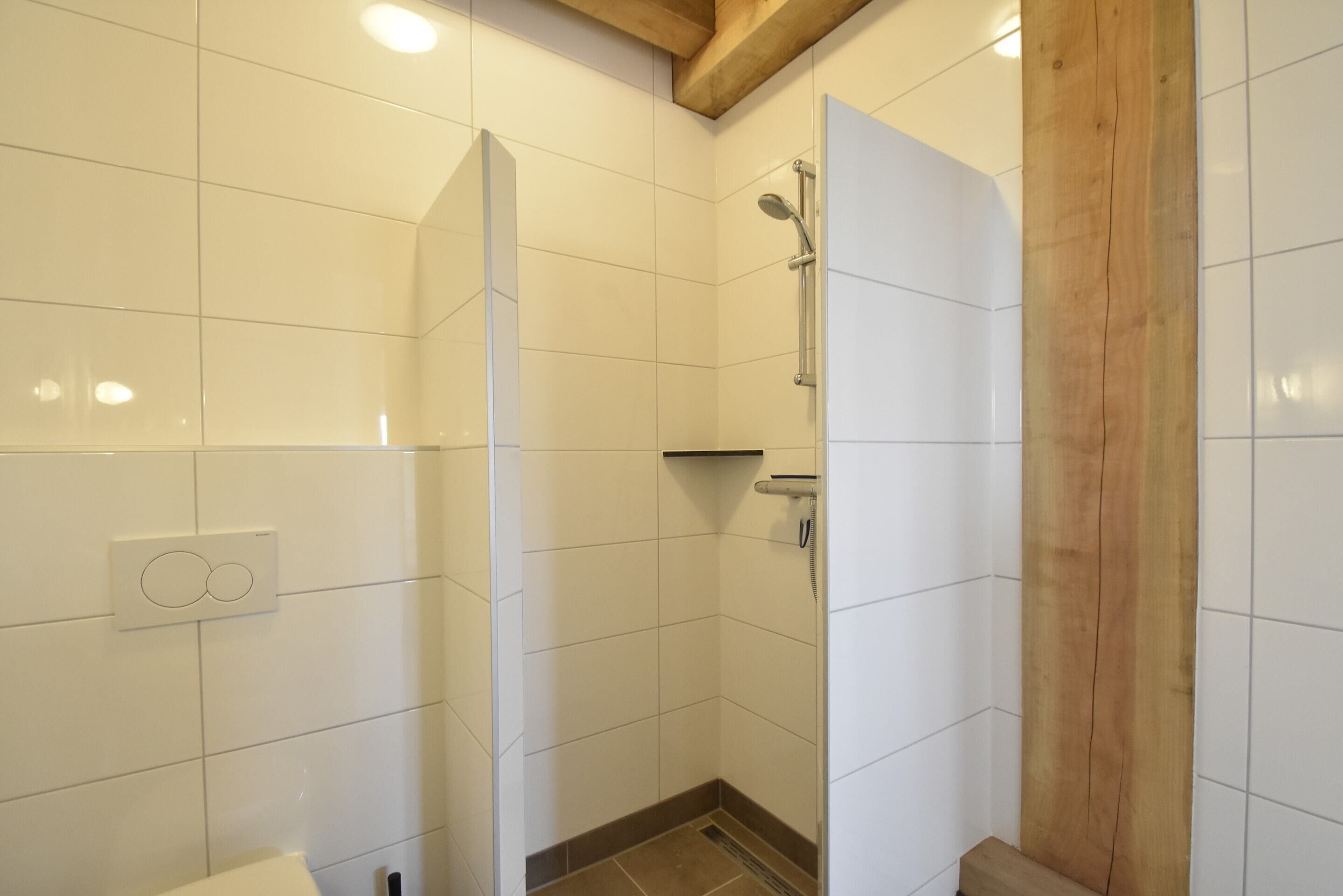 A small, tiled shower area with a wooden beam ceiling and a white wall-mounted control panel.