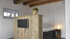 A room with a wooden cabinet, a bed, a TV mounted on the cabinet, and a window with blinds.
