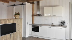 A modern kitchen with white cabinets, a built-in oven, a stainless steel range hood, and a flat-screen TV mounted on a wooden panel.