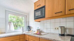 A kitchen with wooden cabinets, a microwave, a coffee maker, and a kettle. - Apartment in Tabarz Near Thuringian Forest (Waltershausen)