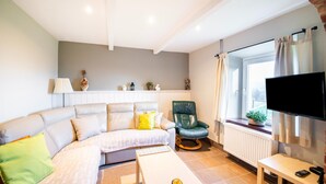 Een moderne woonkamer met een bank, een groene stoel, een salontafel, een televisie en een raam met gordijnen.