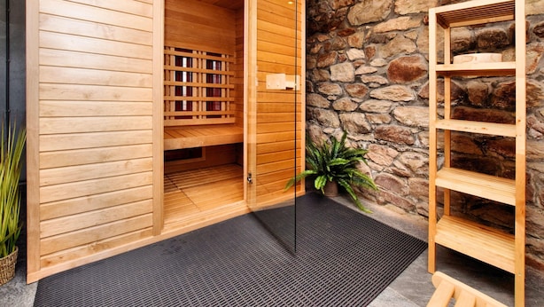 Een houten sauna met een stenen muur, een houten bank en een potplant.