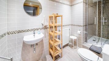 A modern bathroom with a white sink, wooden shelves, a glass shower enclosure, and a toilet.