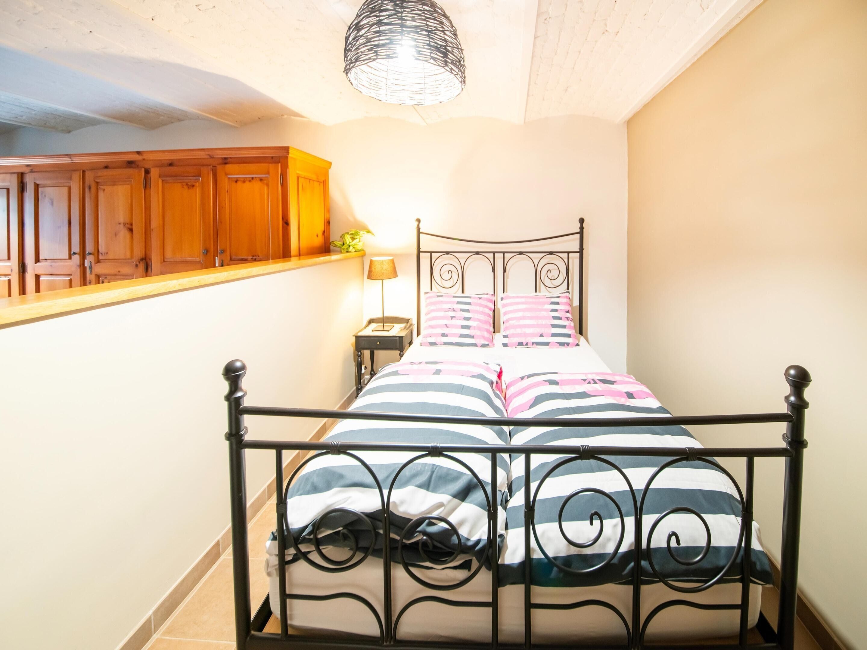 A bedroom with a metal bed frame, a bedside table with a lamp, wooden cabinets, and a hanging light fixture.