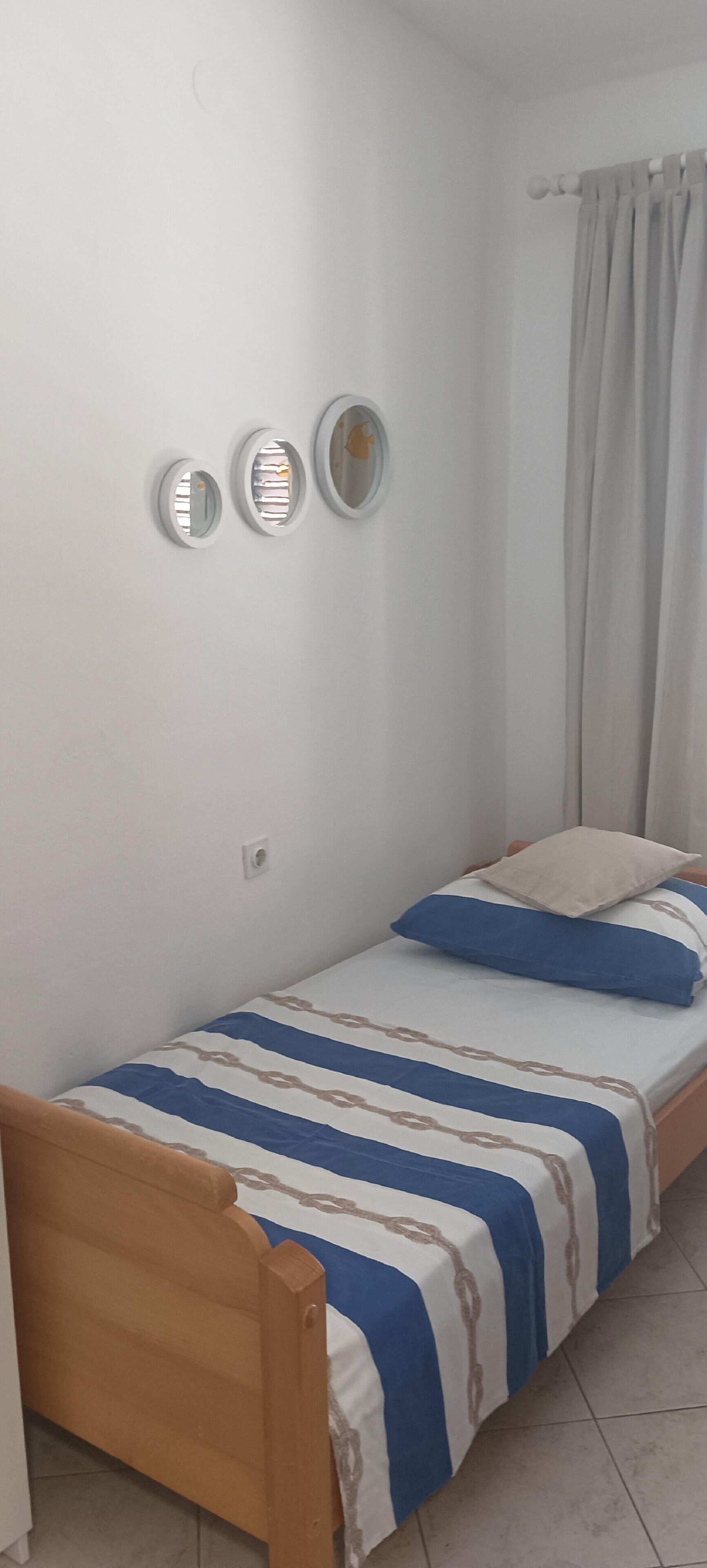 A single bed with a striped bedspread, a wooden headboard, and a curtain on the window.
