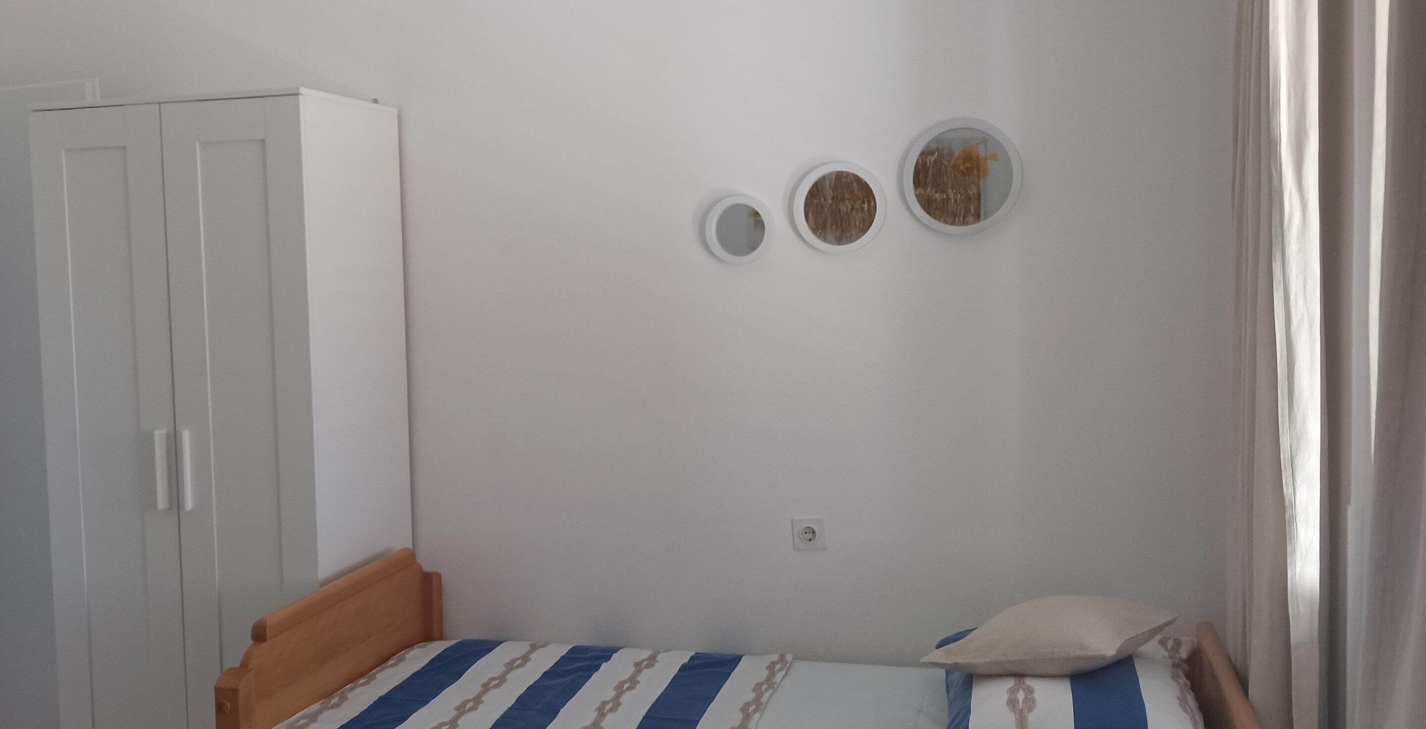 A small bedroom with a single bed, a wardrobe, and three wall-mounted circular mirrors.