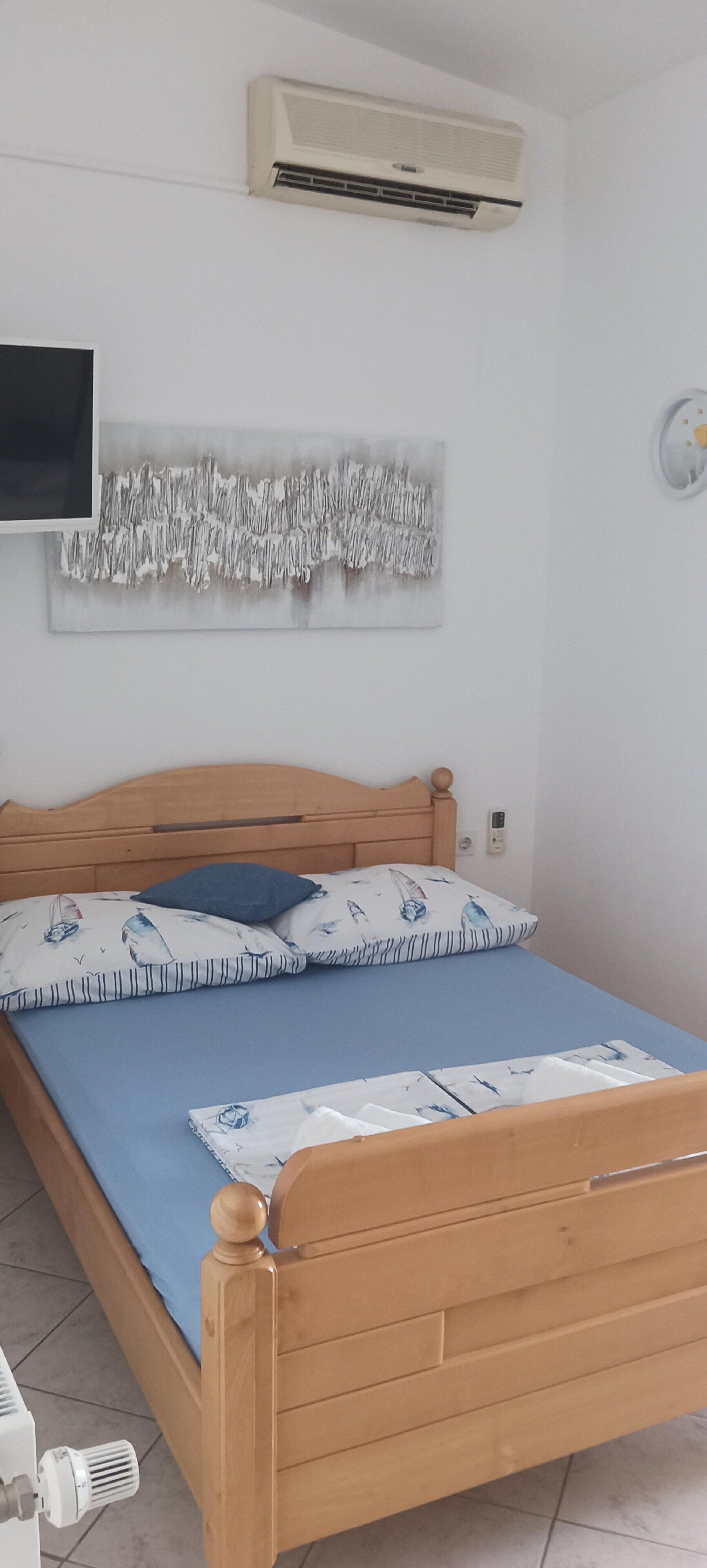 A bedroom with a wooden bed, a blue mattress, and a wall-mounted air conditioner.