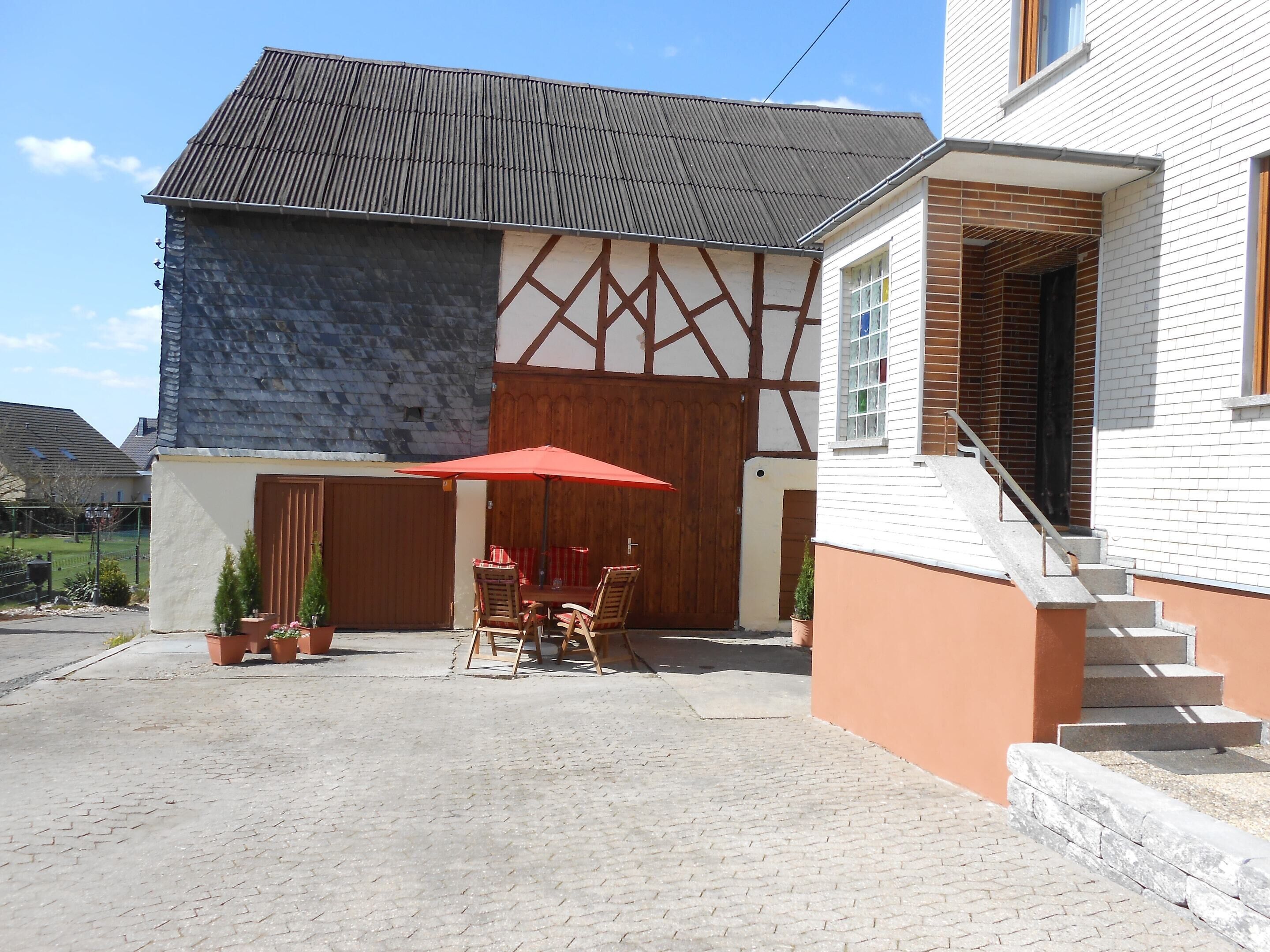 A building with a stone facade, a wooden door, and a red umbrella over a table and chairs.