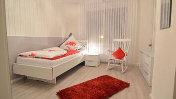 Un dormitorio moderno con cama, alfombra roja, una silla y una mesita de noche.