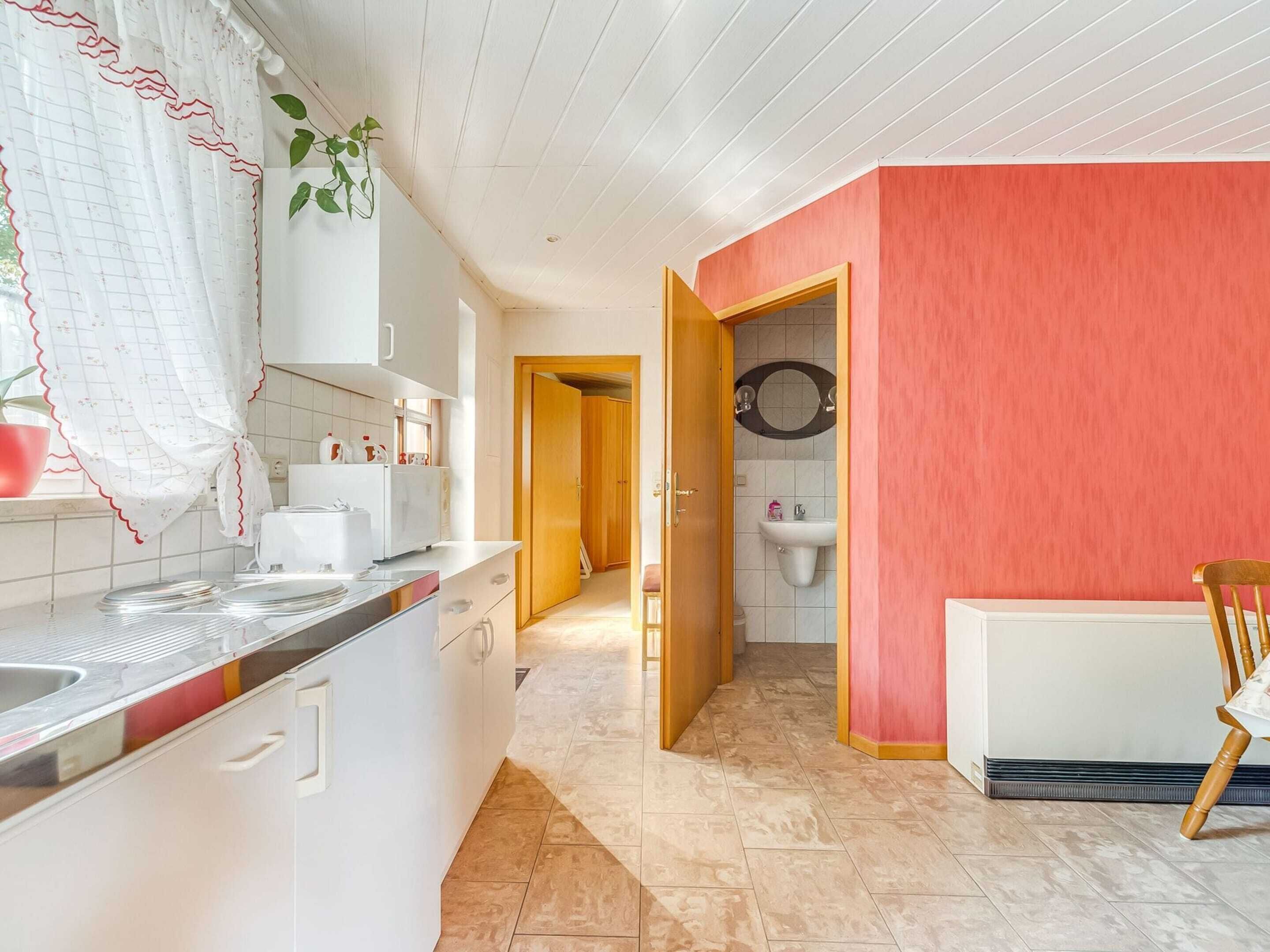 Une cuisine moderne avec des armoires blanches, un plan de travail et un évier. Une porte en bois donne accès à une salle de bain équipée d’un évier blanc et d’un miroir.