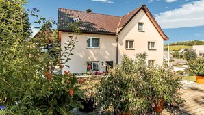 A two-story house with a tiled roof and a garden with potted plants.