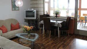 A living room with a sofa, a glass coffee table, a dining table with chairs, a television on a stand, and a window with curtains. - Welcoming Chalet near Forest in Rohrnbach (Roehrnbach)