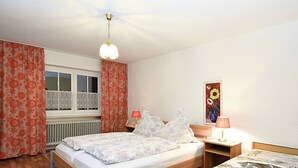 A bedroom with a wooden bed, a nightstand with a lamp, a window with curtains, and a painting on the wall. - Welcoming Chalet near Forest in Rohrnbach (Roehrnbach)
