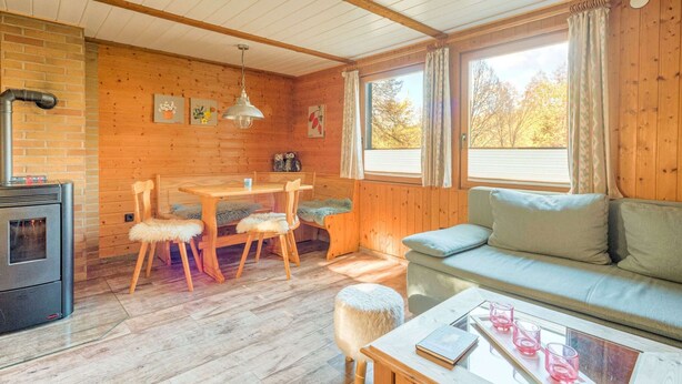 L’intérieur d’un chalet accueillant, avec une table à manger en bois, des chaises, un canapé et une table basse en verre.