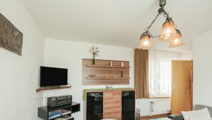 A modern living room with a flat-screen TV, a wooden entertainment unit, a sofa, a dining table, and a decorative hanging light fixture. - Gartenwohnung in Ilsenburg (Ilsenburg)