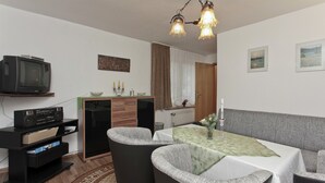 A dining area with a table set for four, a television on a stand, and a cabinet with drawers. - Gartenwohnung in Ilsenburg (Ilsenburg)