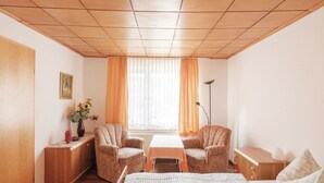 A room with a bed, two armchairs, a small table, a vase with flowers, a floor lamp, and a window with curtains. - Gartenwohnung in Ilsenburg (Ilsenburg)