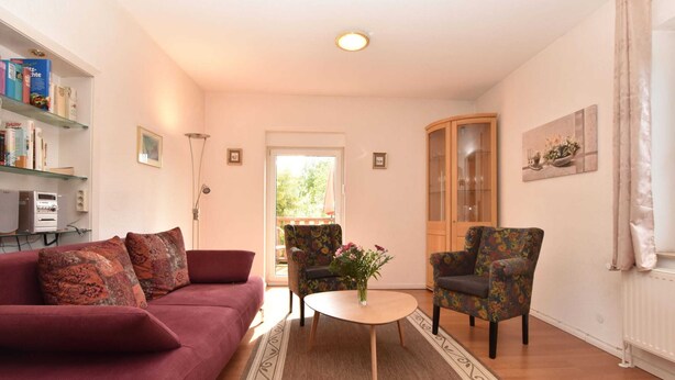 A living room with a red sofa, a floral armchair, a coffee table, and a bookshelf. - Quaint Apartment in Rerik near Sea (Rerik)