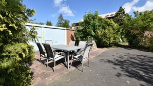 A patio with a table and chairs, surrounded by greenery and a building in the background. - Quaint Apartment in Rerik near Sea (Rerik)