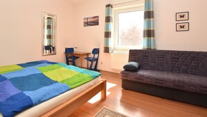 A bedroom with a bed, a sofa, a table, chairs, a window with curtains, and wall art. - Quaint Apartment in Rerik near Sea (Rerik)