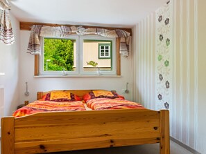 Un dormitorio con cama de madera, cortinas a rayas, ventana con vistas a vegetación y papel tapiz floral.